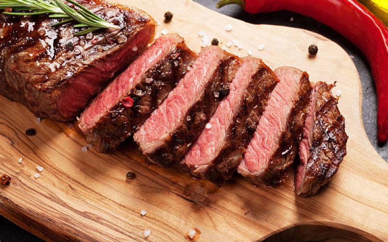 Grilled striploin sliced steak on cutting board over stone table